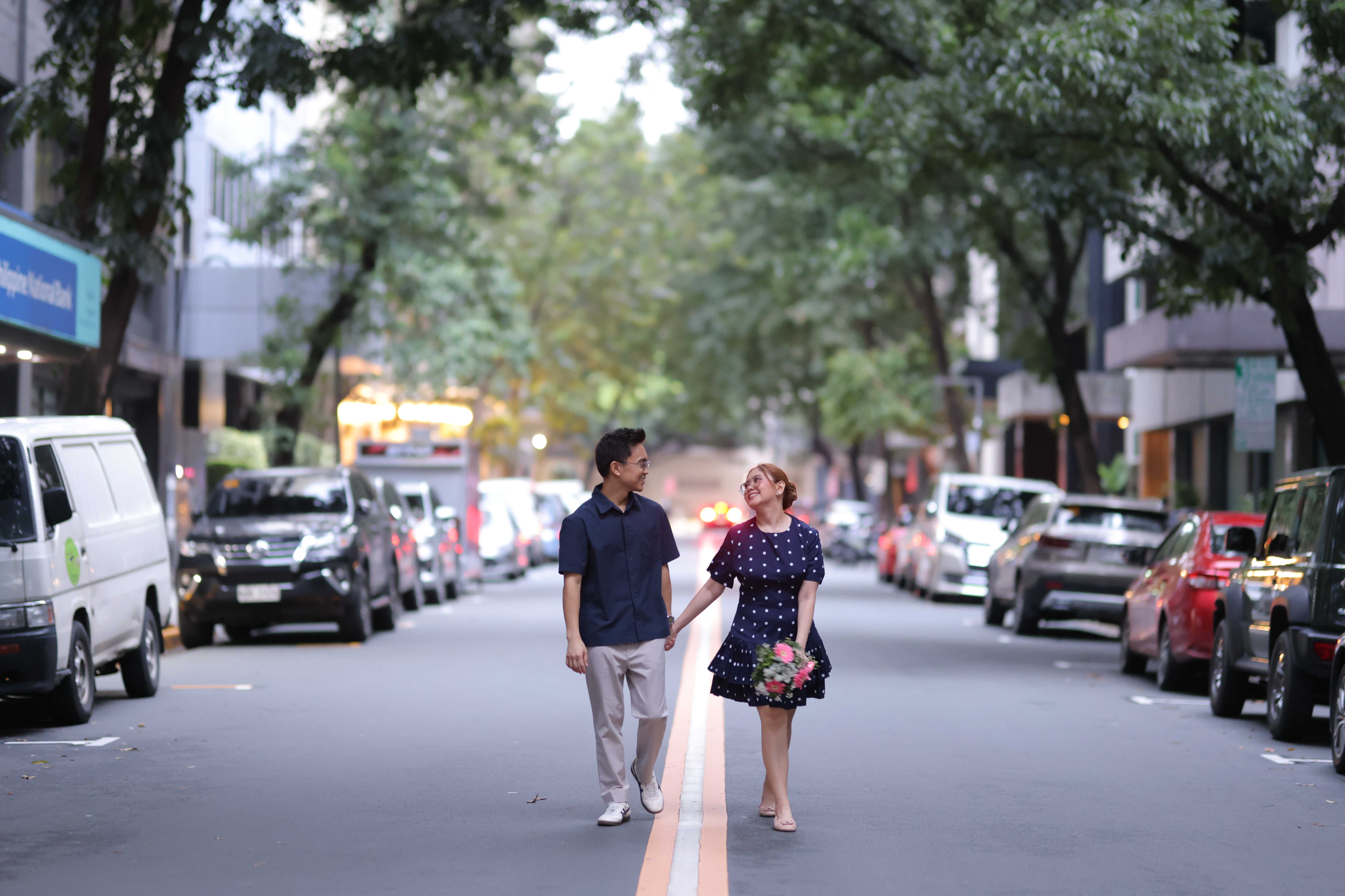 The couple walking hand in hand down a tree-lined Makati street