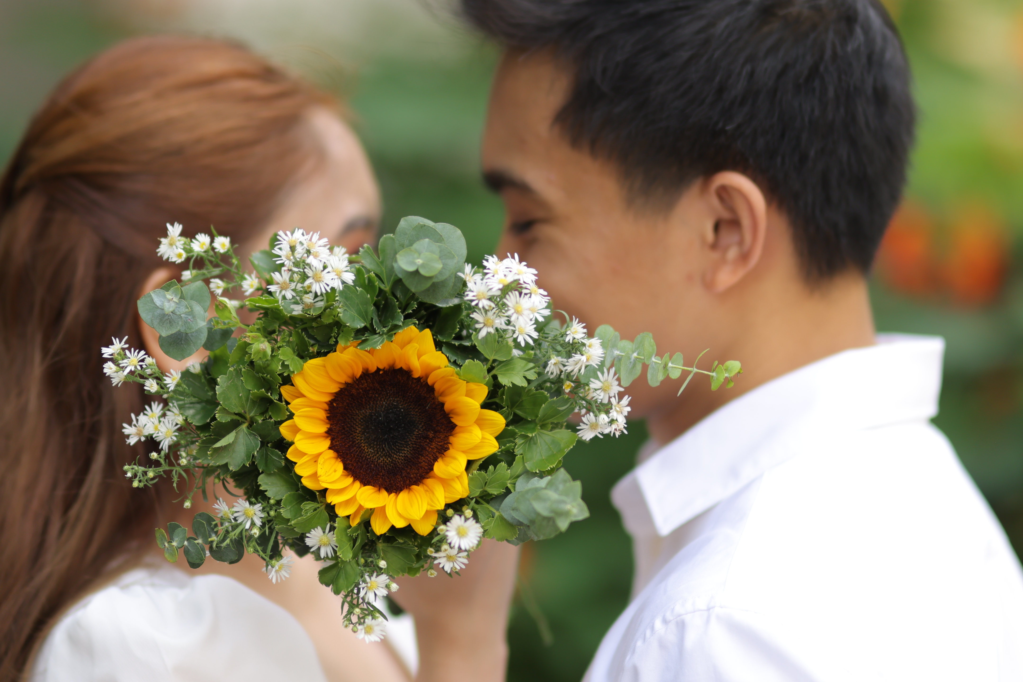 Joel and Irianne leaning close behind a sunflower bouquet